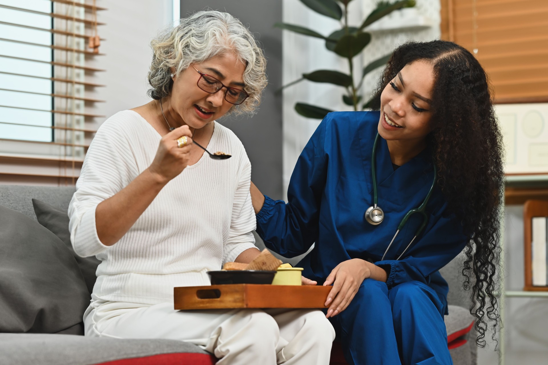 An African Female caregiver serving food to the senior woman in the nursing home. Caring for the elderly people and nursing home concepts